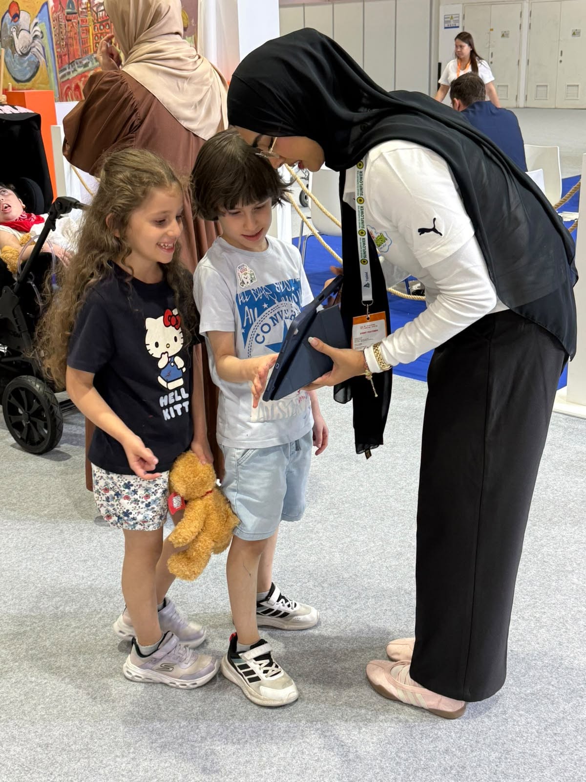 A Down Syndrome Digital team member demonstrates 321 Playsy on a tablet to two young visitors.