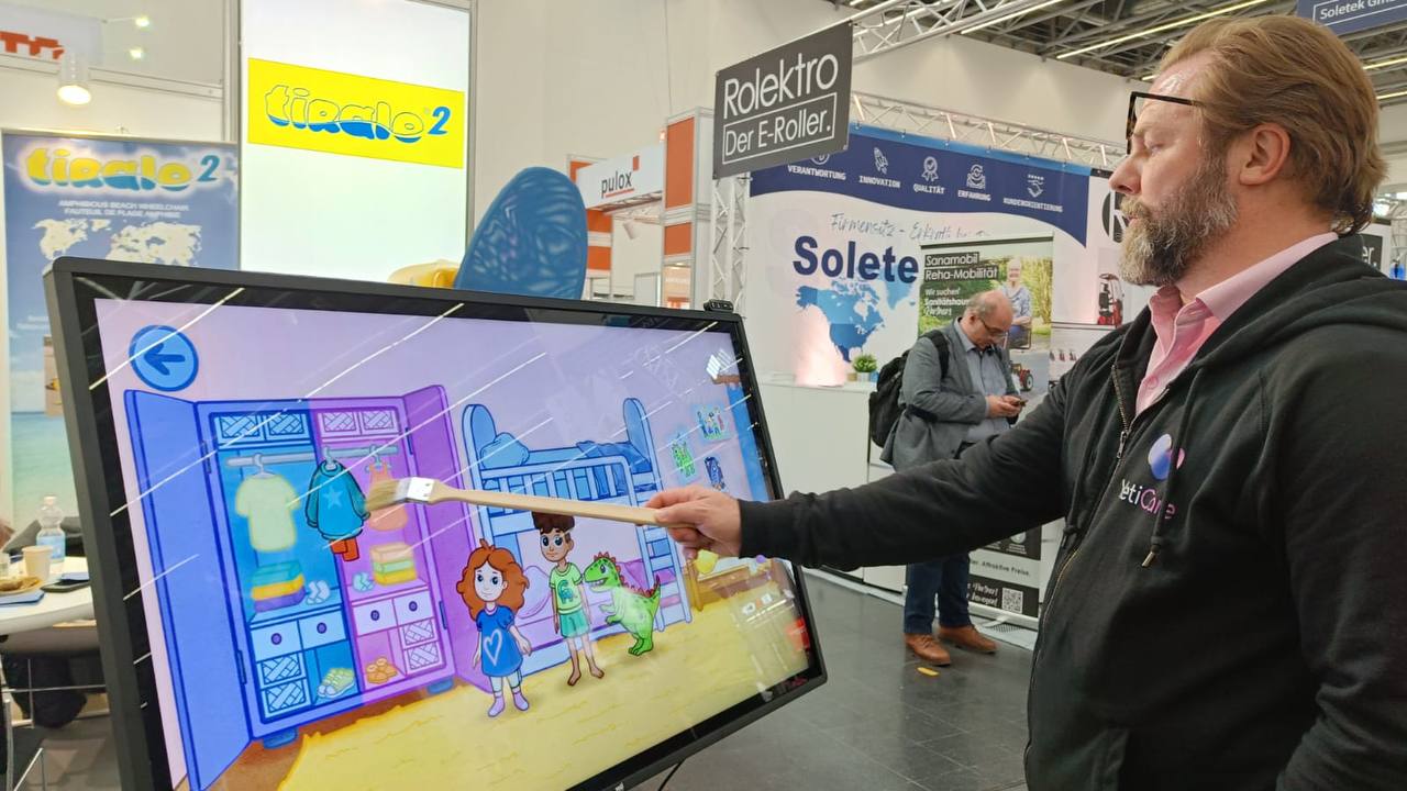 A REHACARE 2026 visitor exploring 321Playsy on a large touchscreen at an exhibitor stand.