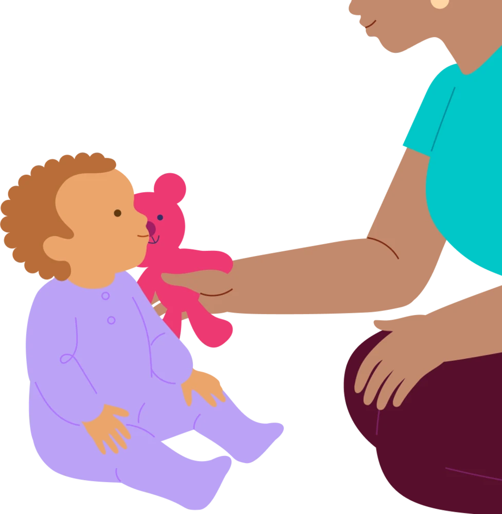 A caregiver offers a soft toy while staying close to a baby playing on the floor.